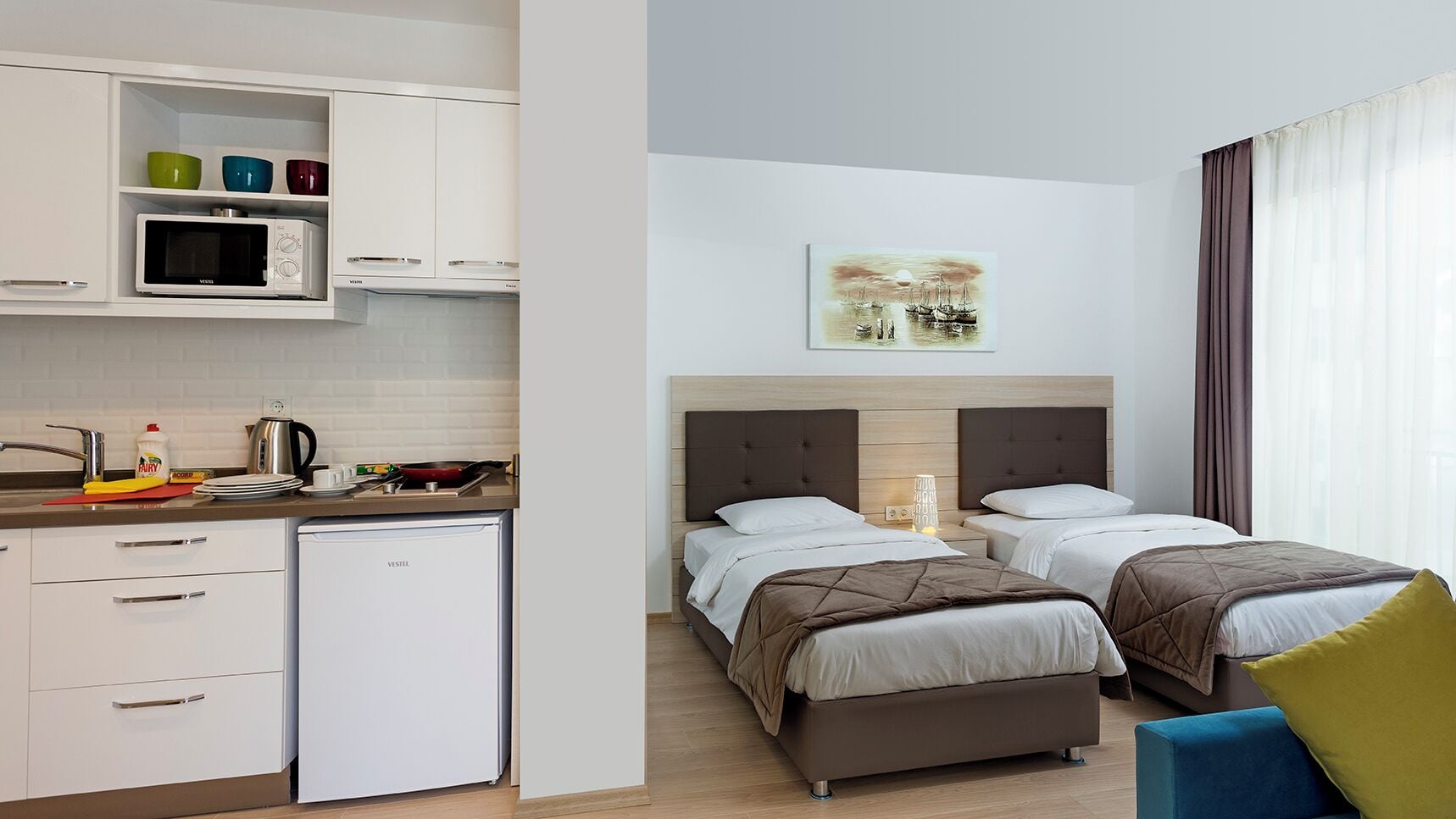 Une chambre d’hôtel avec deux lits, une kitchenette et un tableau au mur.