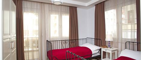 A bedroom with two beds, a bedside table, a lamp, and a window with curtains.