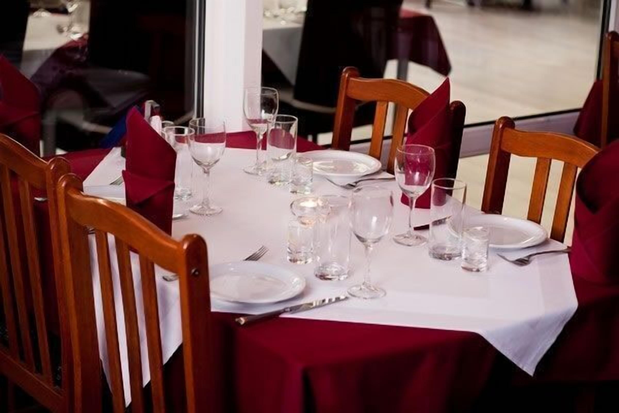 Mesa de comedor lista para seis personas, con mantel blanco y servilletas rojas.