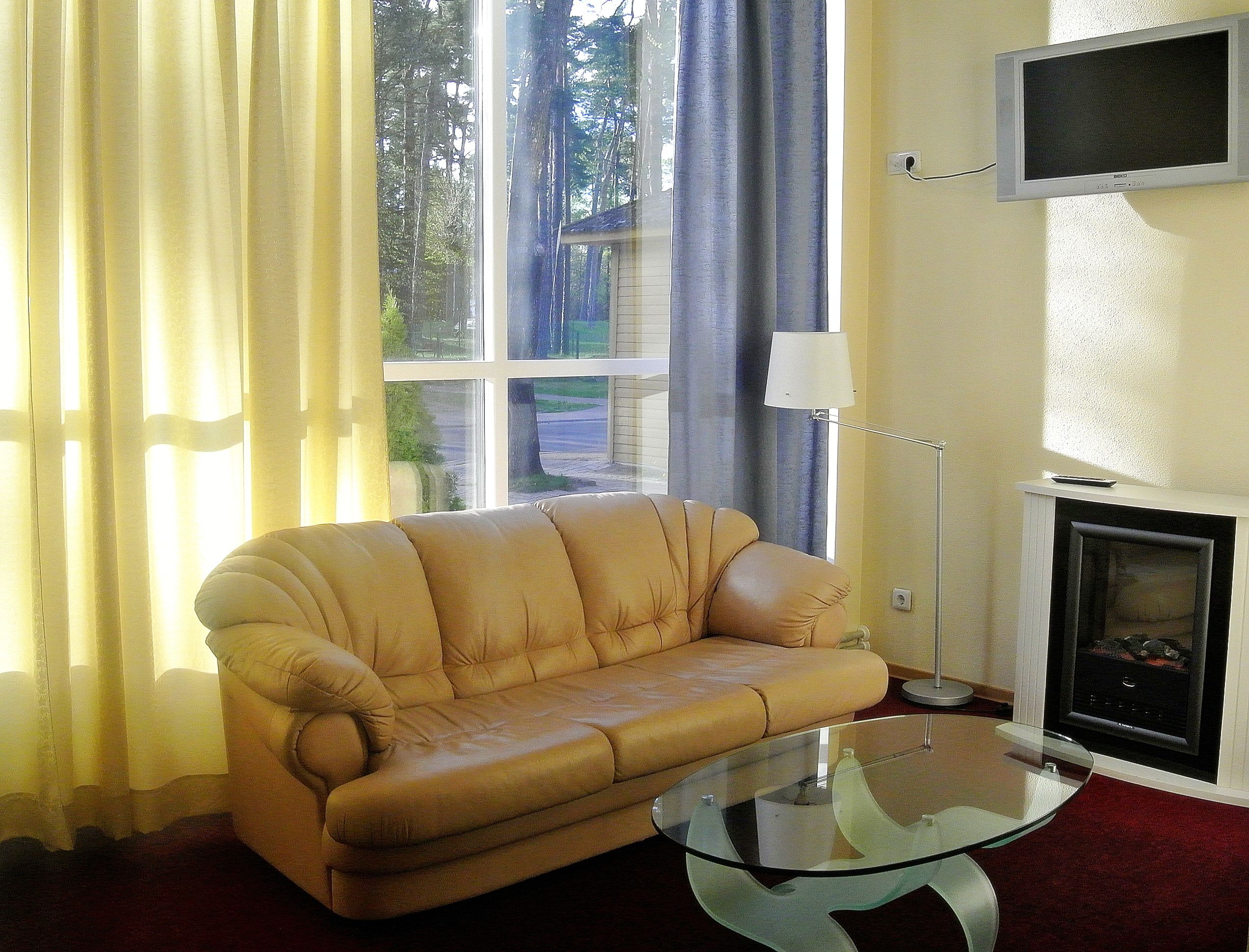 A living room with a beige sofa, a glass coffee table, a TV mounted on the wall, and a fireplace.