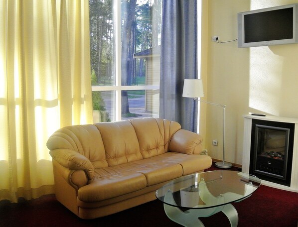 Una sala de estar con un sofá beige, una mesa de centro de vidrio, un televisor montado en la pared y una chimenea.