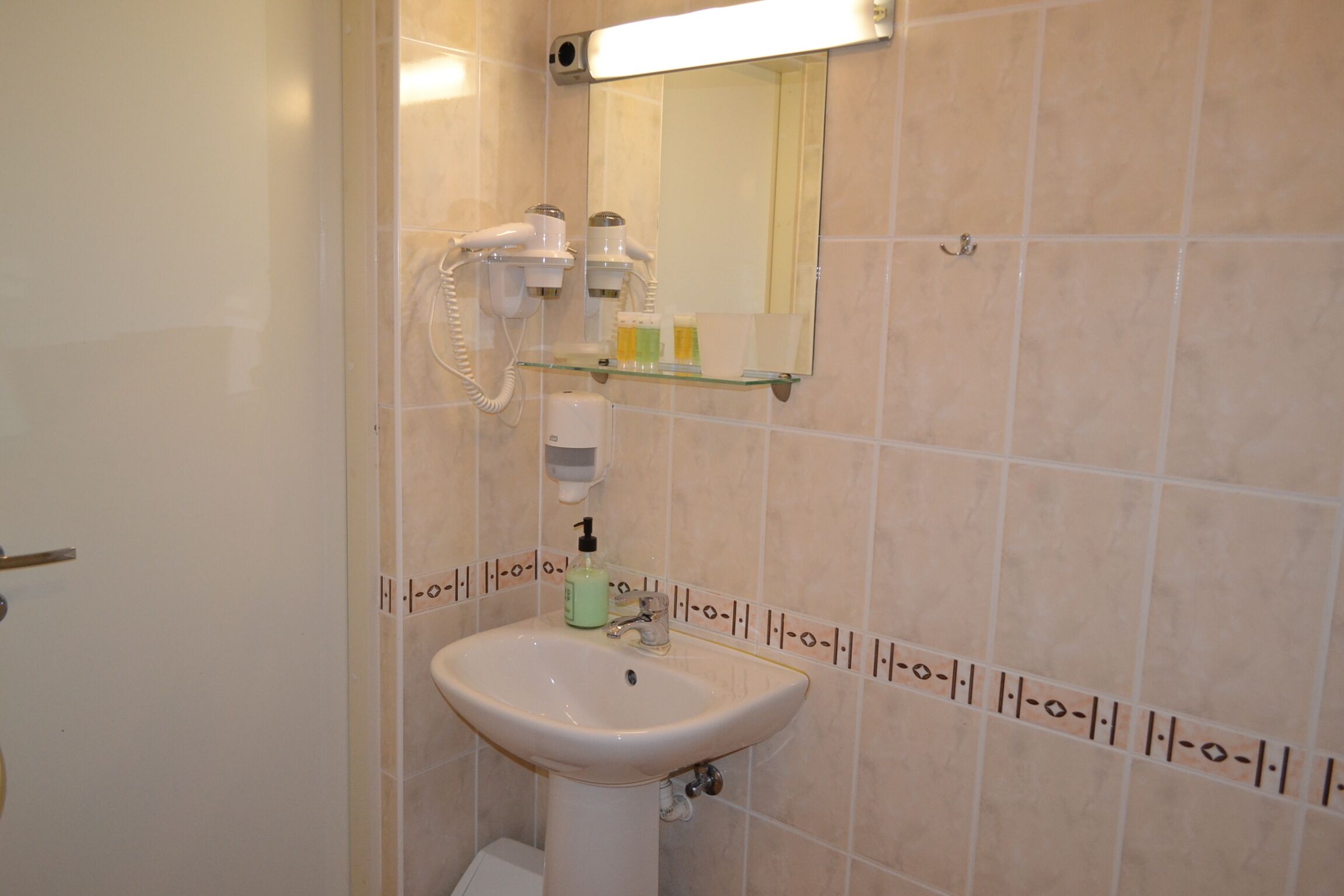 A bathroom with a sink, a mirror, and a hairdryer on a wall-mounted shelf.