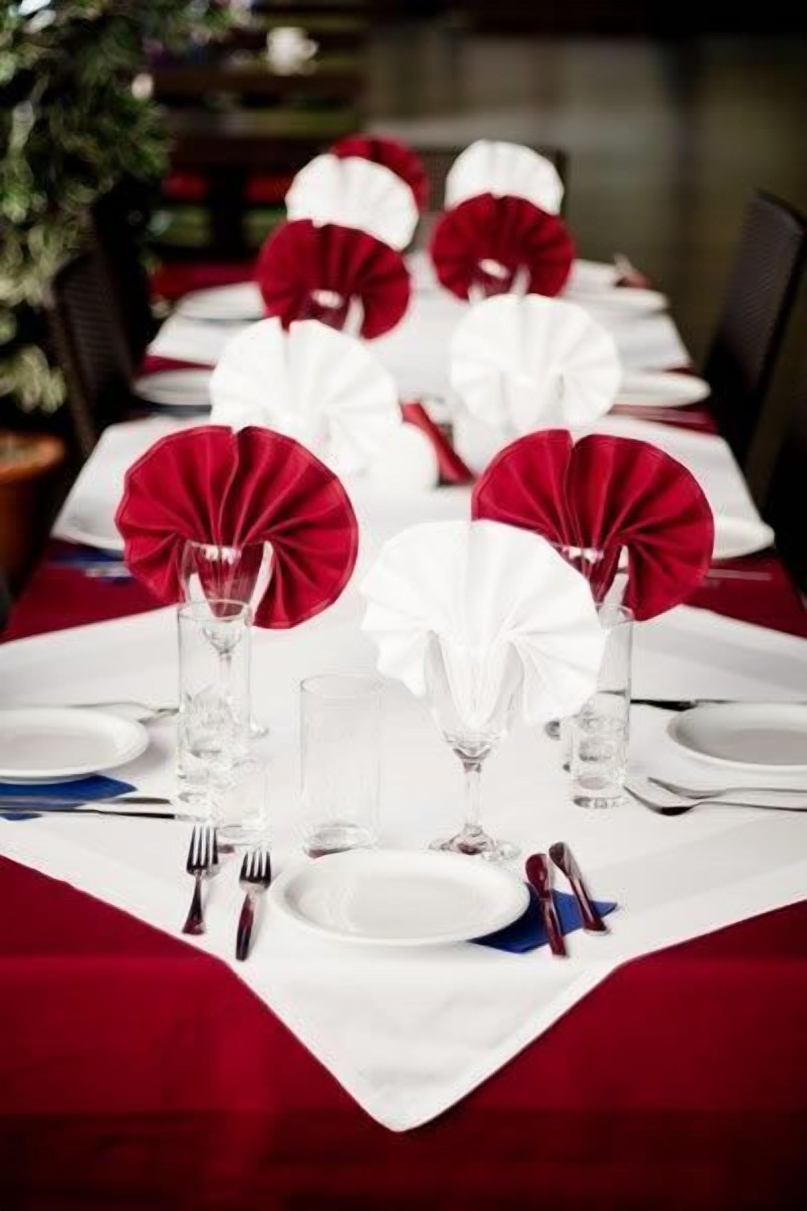 Een eettafel gedekt met witte tafelkleden, rode en witte servetten en glazen.