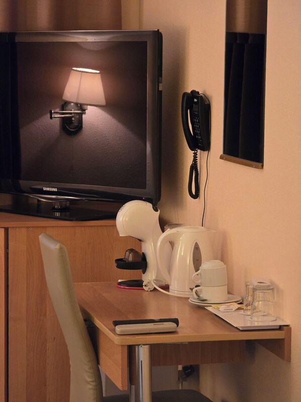 Habitación de hotel con televisión, teléfono, cafetera, una silla y un escritorio.