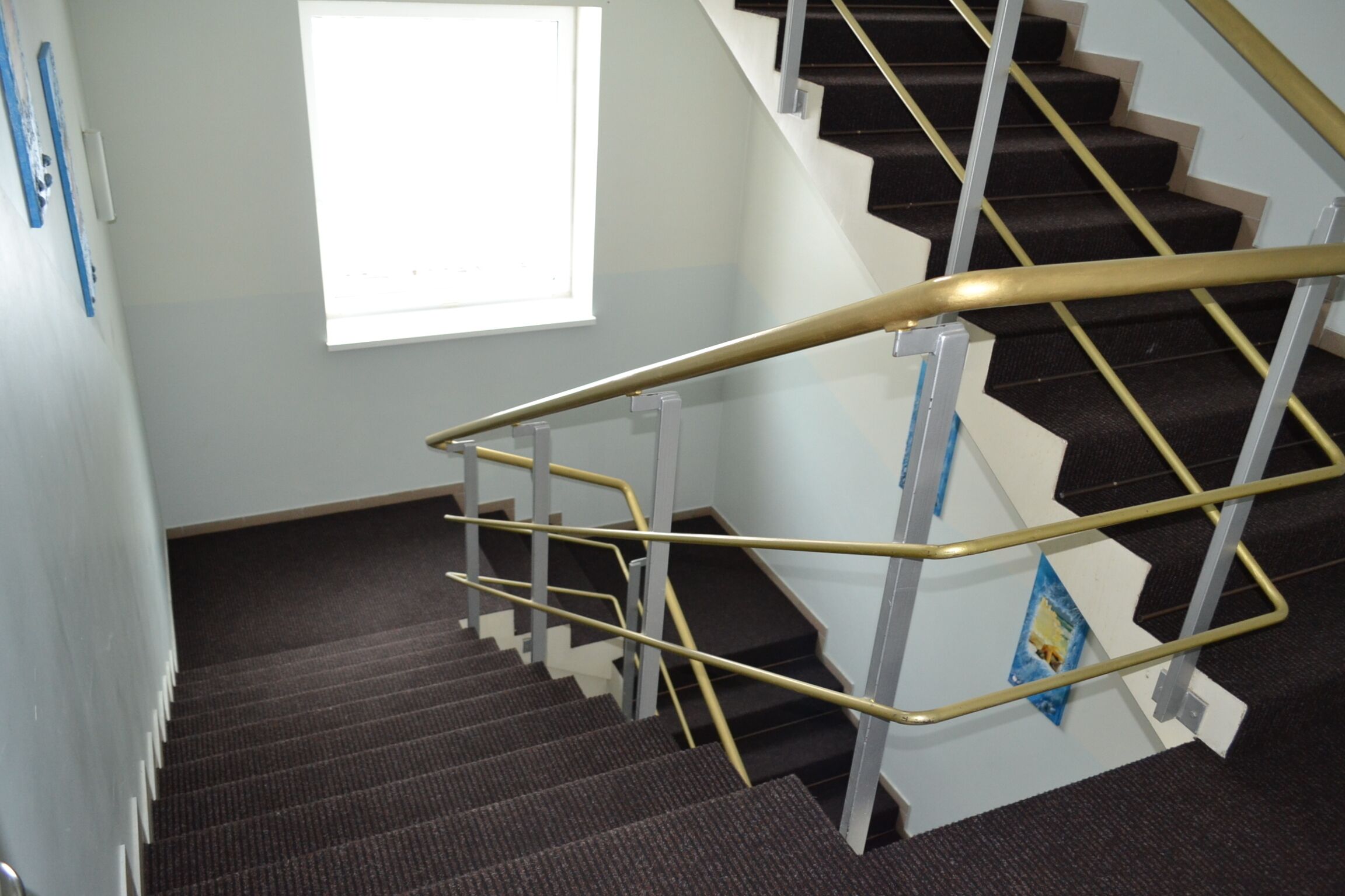 A staircase with a handrail, carpeted steps, and a window with blinds.