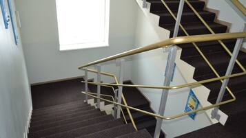 A staircase with a handrail, carpeted steps, and a window with blinds.