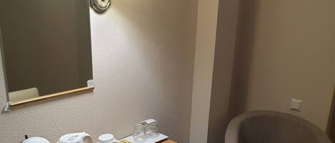 Habitación de hotel con una mesa de madera, dos sillas, un hervidor, una cafetera, un espejo y dos lámparas fijadas a la pared.