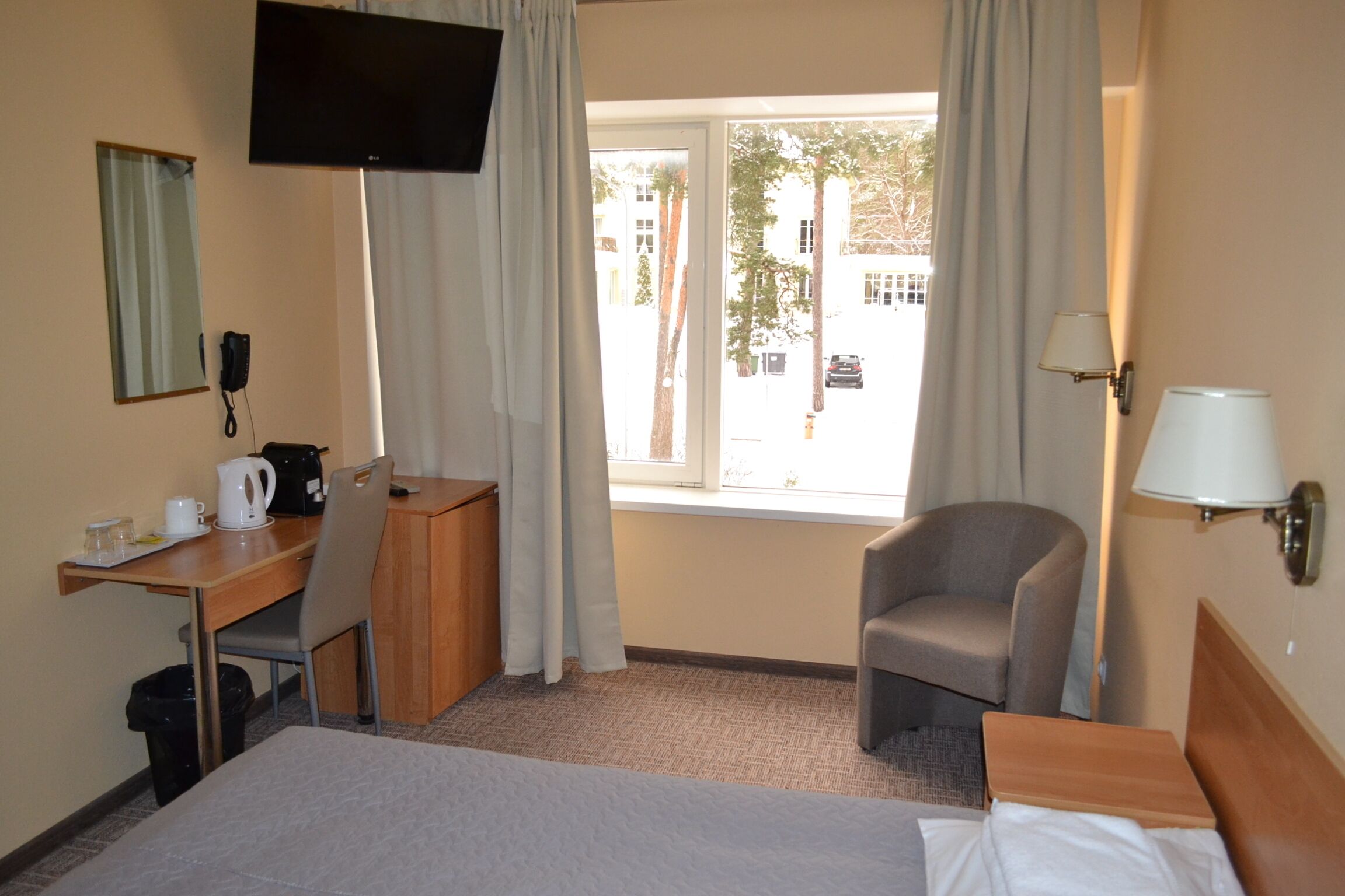 A hotel room with a bed, a desk with a telephone, a chair, a television, and a window with curtains.