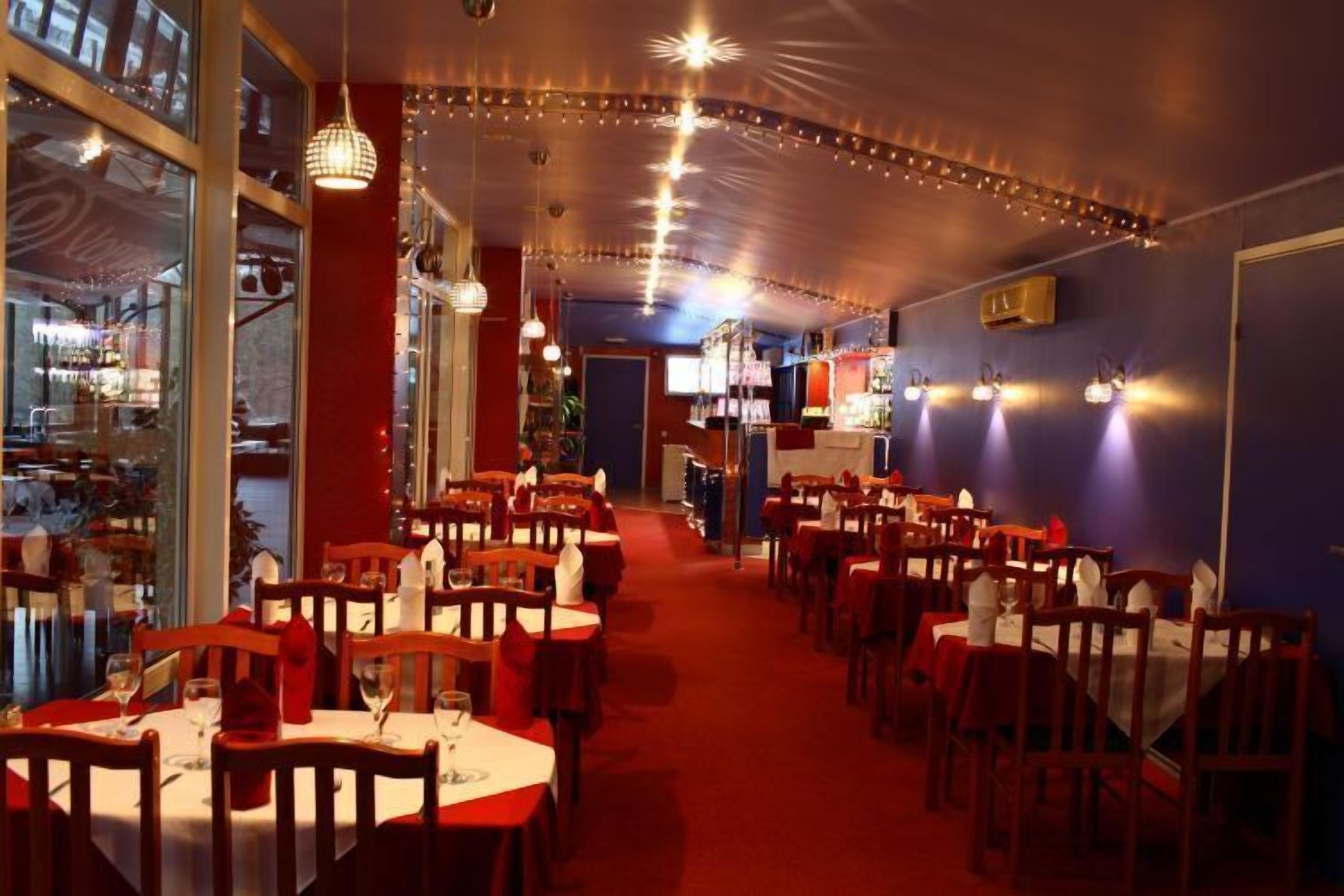 A restaurant with multiple tables and chairs, a red carpet, and string lights on the ceiling.