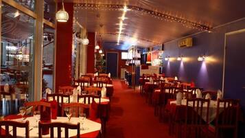 A restaurant with multiple tables and chairs, a red carpet, and string lights on the ceiling.