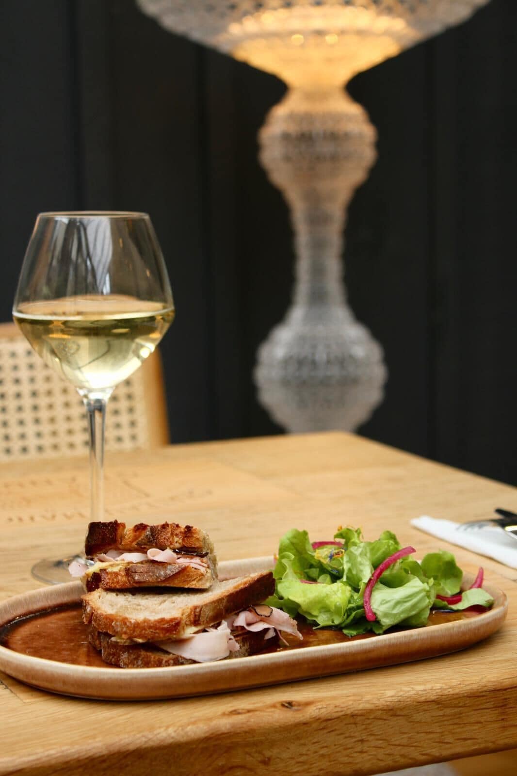 Un plato con un sándwich y una copa de vino blanco sobre una mesa de madera.
