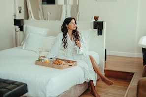 Una persona sentada en una cama con una bandeja de comida, un florero con flores secas y una bandeja de madera.