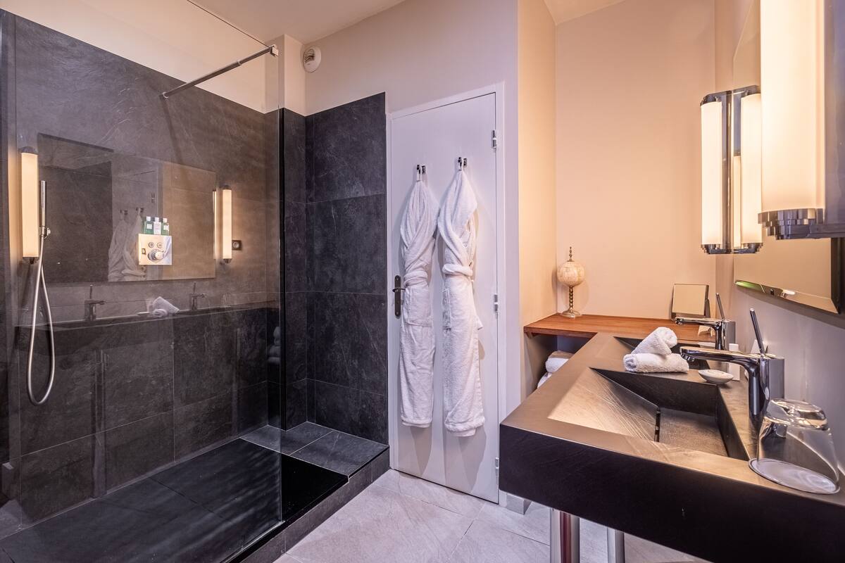 A modern bathroom with a glass-enclosed shower, a vanity with a sink and mirror, and two towels hanging on a door.