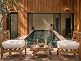 A wooden deck with a pool, two chairs, and a table with breakfast items.