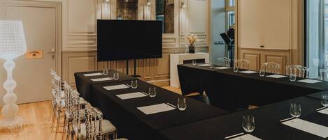 Un salón de conferencias con una larga mesa, sillas, un televisor y un elemento decorativo en la pared.
