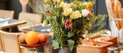A breakfast setting with a vase of flowers, fruit bowl, juice pitchers, and bread.