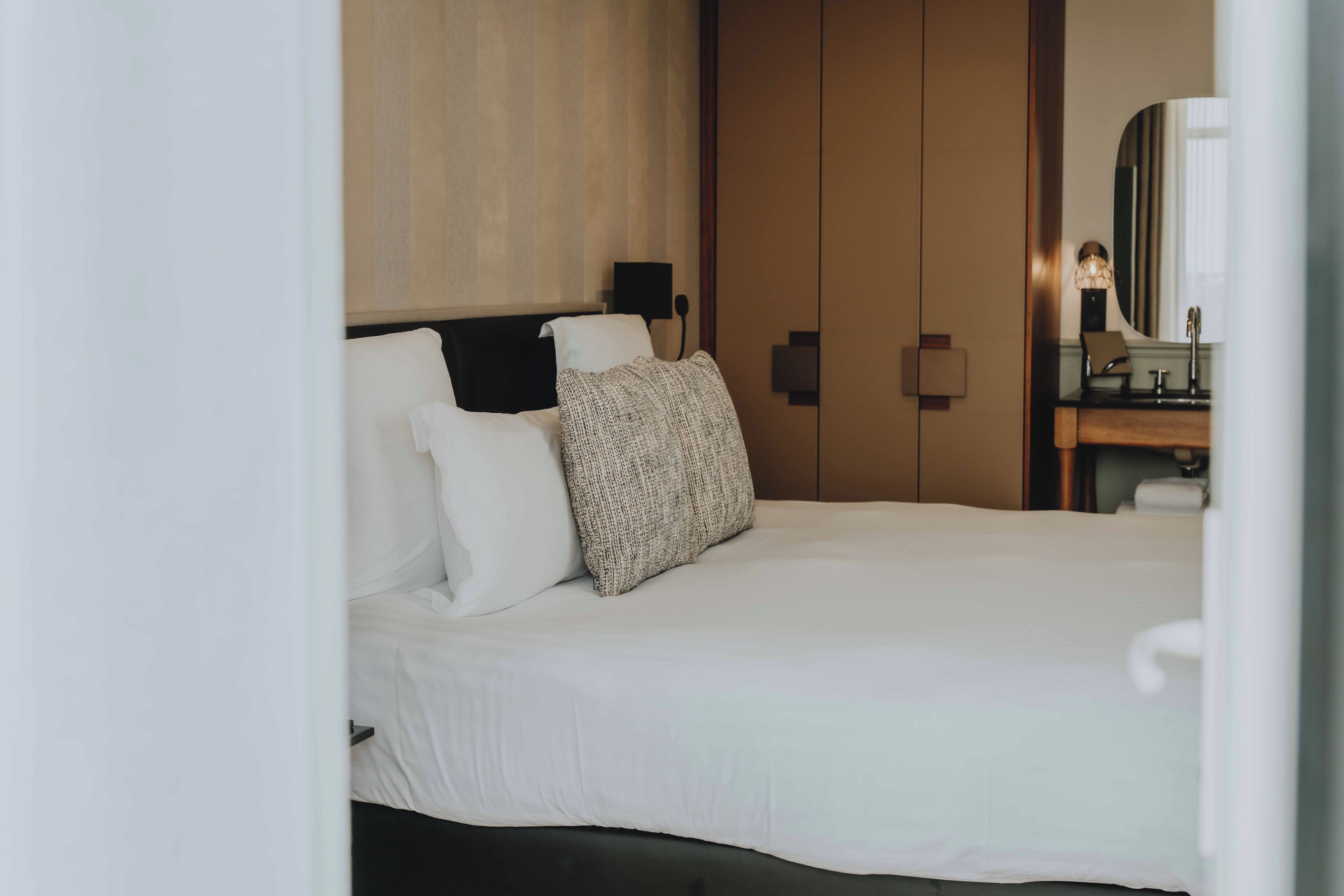 A hotel room with a bed, a nightstand, a mirror, and a door.