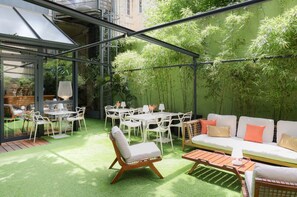 A patio area with a glass enclosure, outdoor seating, and lush greenery.