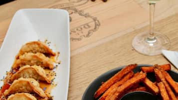 Uma mesa com um prato de comida, um copo de vinho e a mão de uma pessoa.