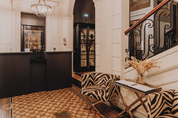 A lobby with a patterned floor, a reception desk, a staircase with ornate railings, and a chandelier. - Le Boutique Hotel & Spa (Bordeaux)