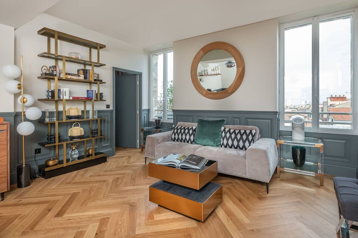 A modern living room with a sofa, a coffee table, a bookshelf, and a large window with a view of buildings.
