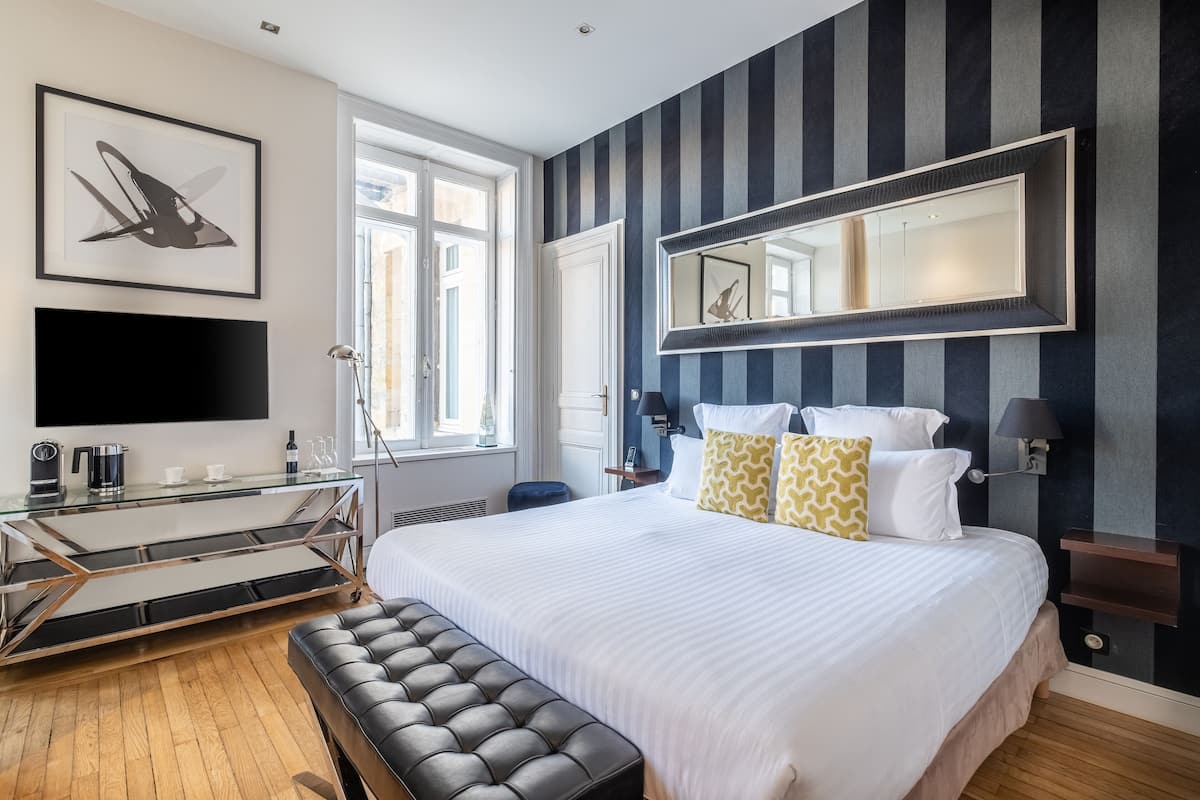 A modern hotel room with a large bed, a flat-screen TV, a glass coffee table, and a large mirror on the wall.