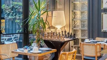 Un coin repas avec des chaises en bois, un jeu d’échecs et une grande plante.