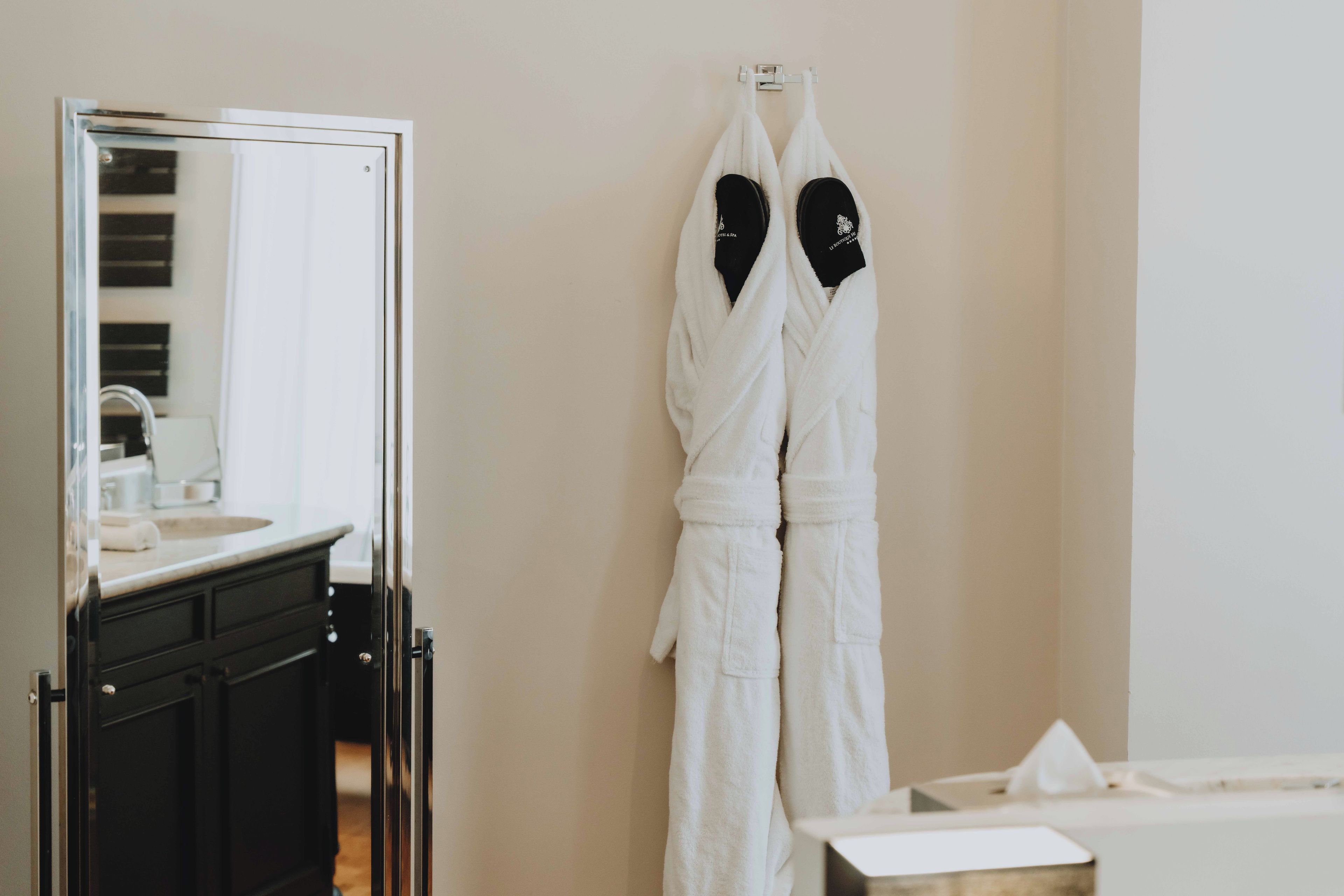 Een badkamer met een spiegel, een wastafel en twee witte badjassen aan een rek.