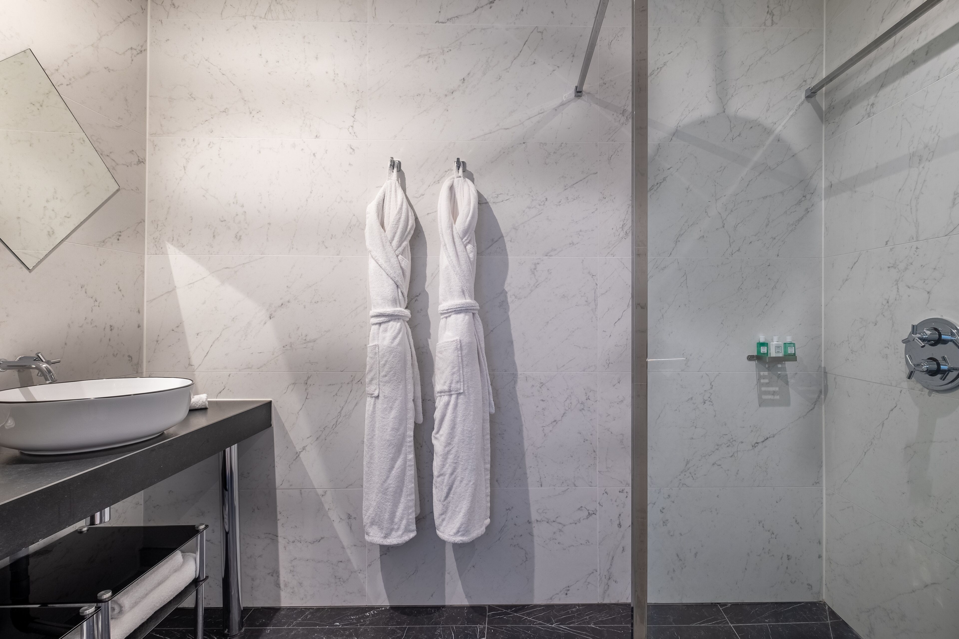 Un baño moderno con un lavamanos grande de color blanco, un box de ducha de vidrio y dos toallas blancas colgadas en ganchos.