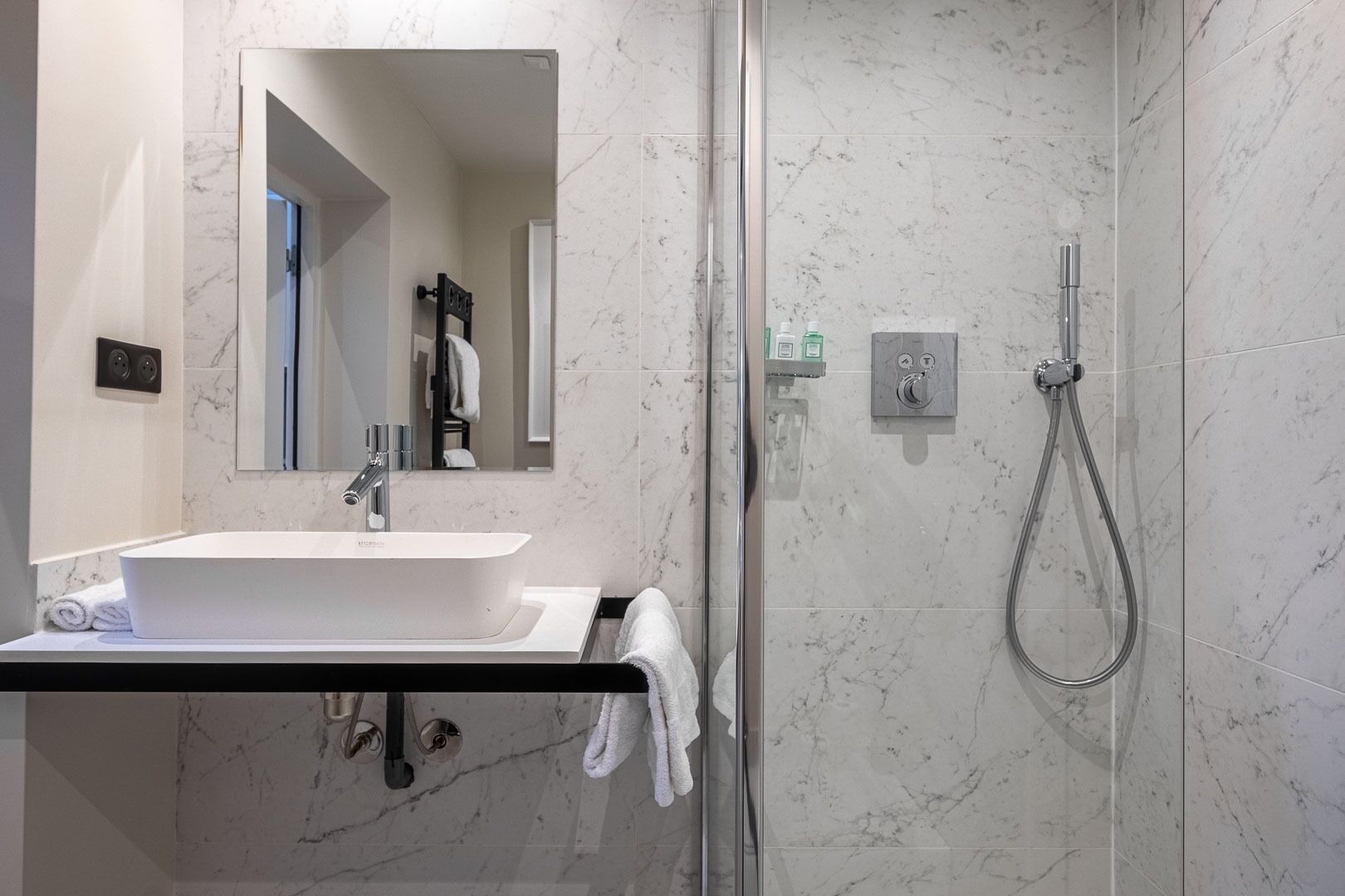 A modern bathroom with a white sink, a mirror, and a glass-enclosed shower.