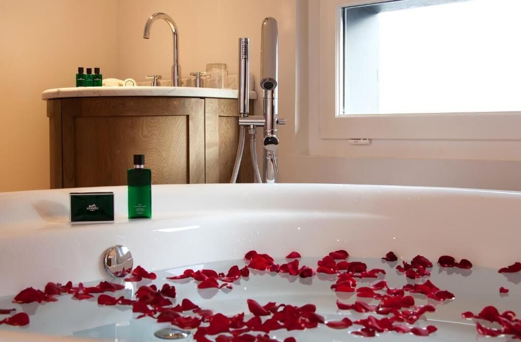 Un baño con una bañera llena de pétalos de rosa, un lavabo con artículos de aseo y una ducha.
