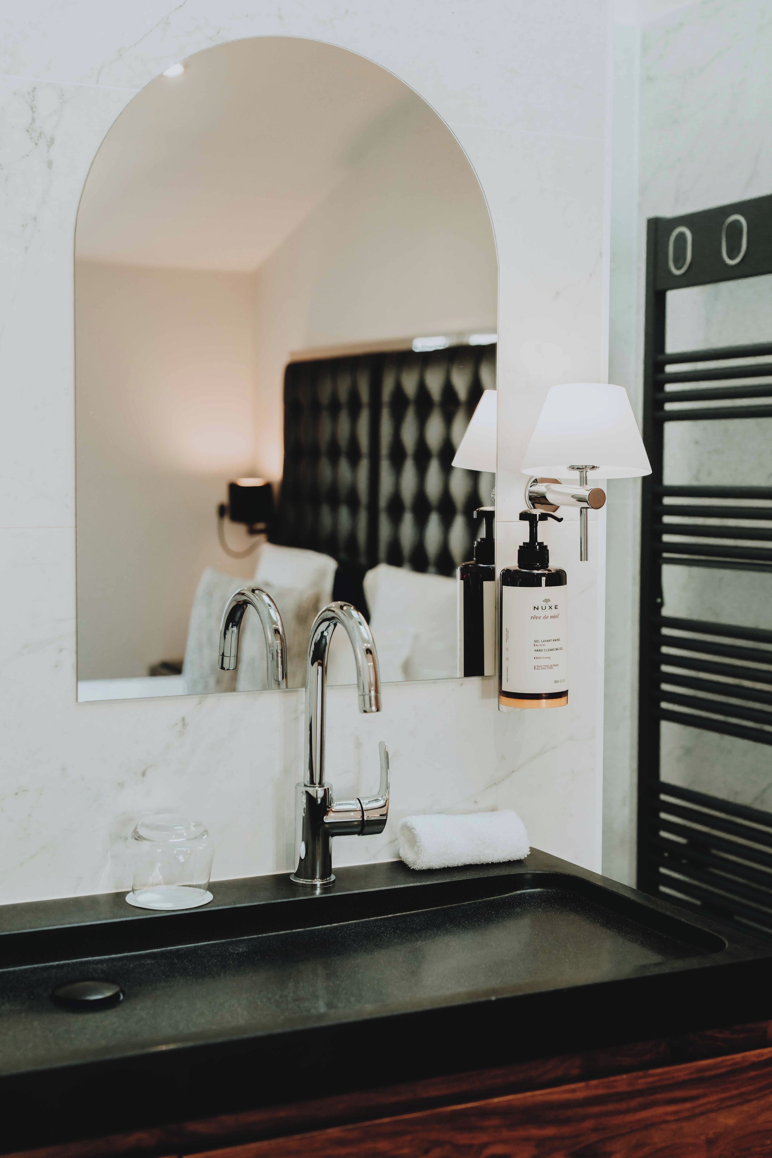 A bathroom with a marble sink, a mirror, a towel, and a hand cleansing gel bottle.
