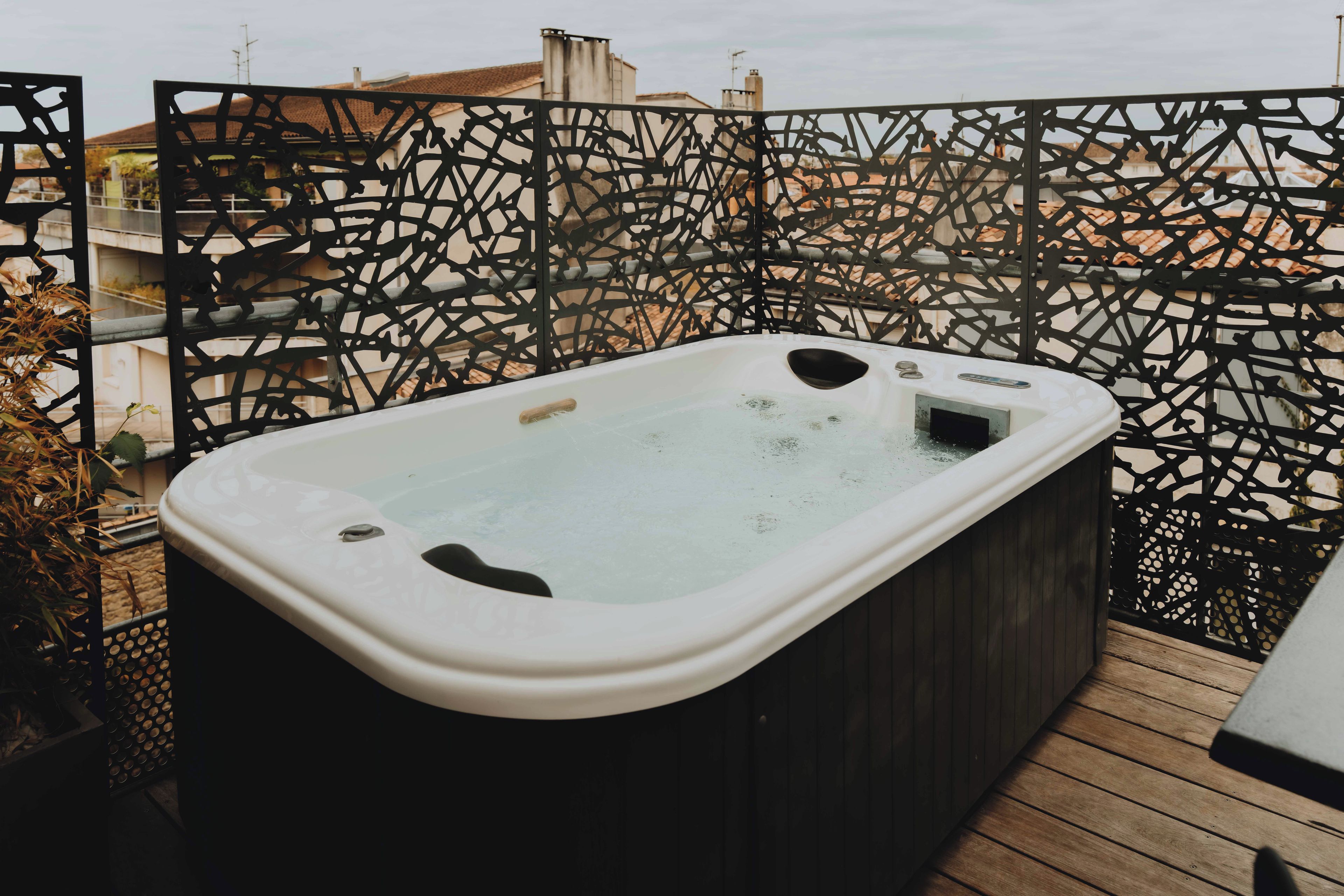 Un bain à remous sur une terrasse en bois, avec une clôture en métal décorative en arrière-plan.