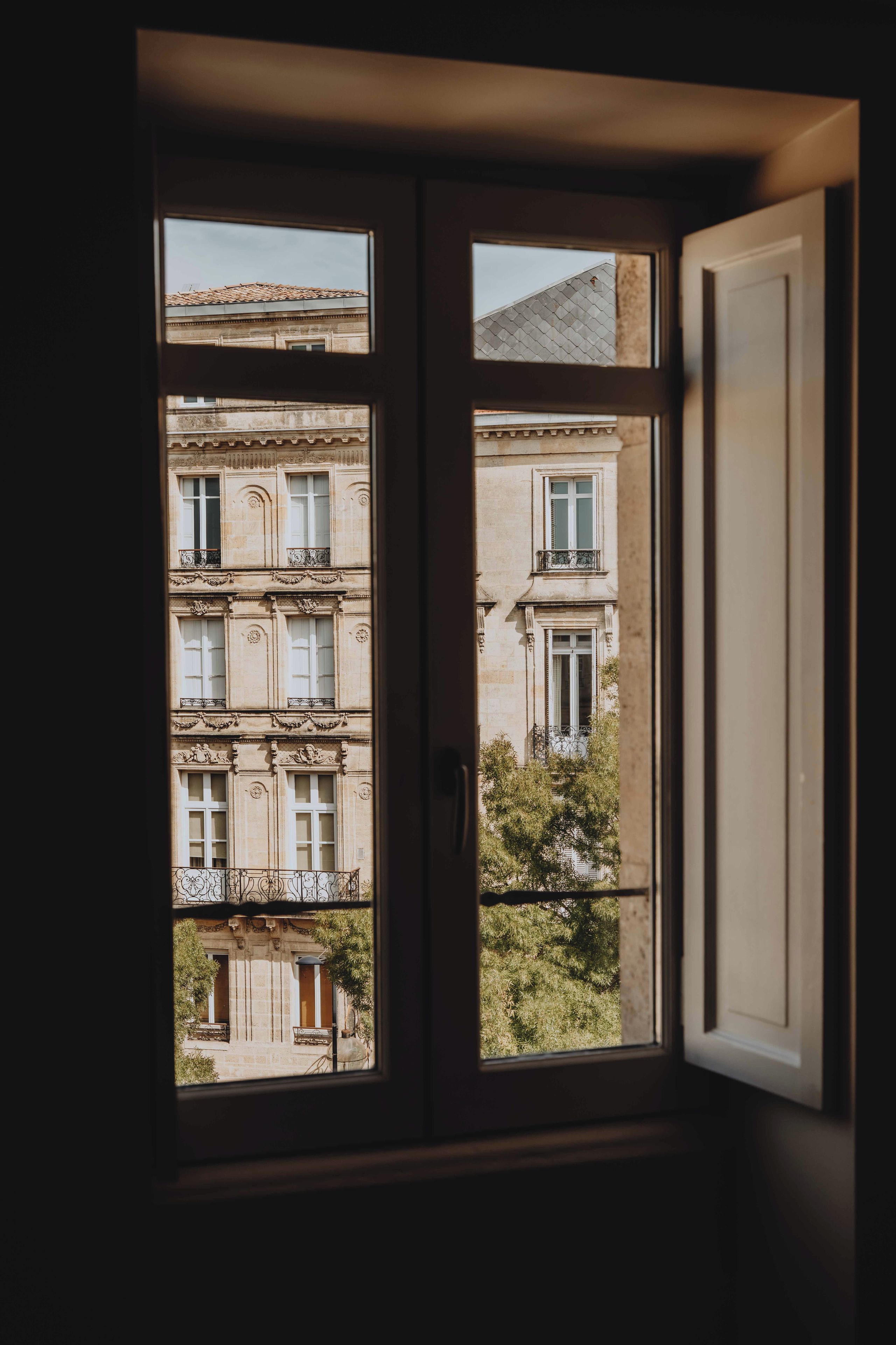 Vista a través de una ventana de un edificio de varios pisos, con balcones con barandillas de hierro forjado y un estilo arquitectónico clásico.