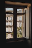 Vista attraverso una finestra di un edificio a più piani, con balconi dotati di ringhiere in ferro battuto e uno stile architettonico classico.