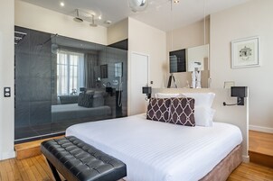 Quarto de hotel moderno com uma cama grande, chuveiro separado, toucador com espelho e um quadro na parede.