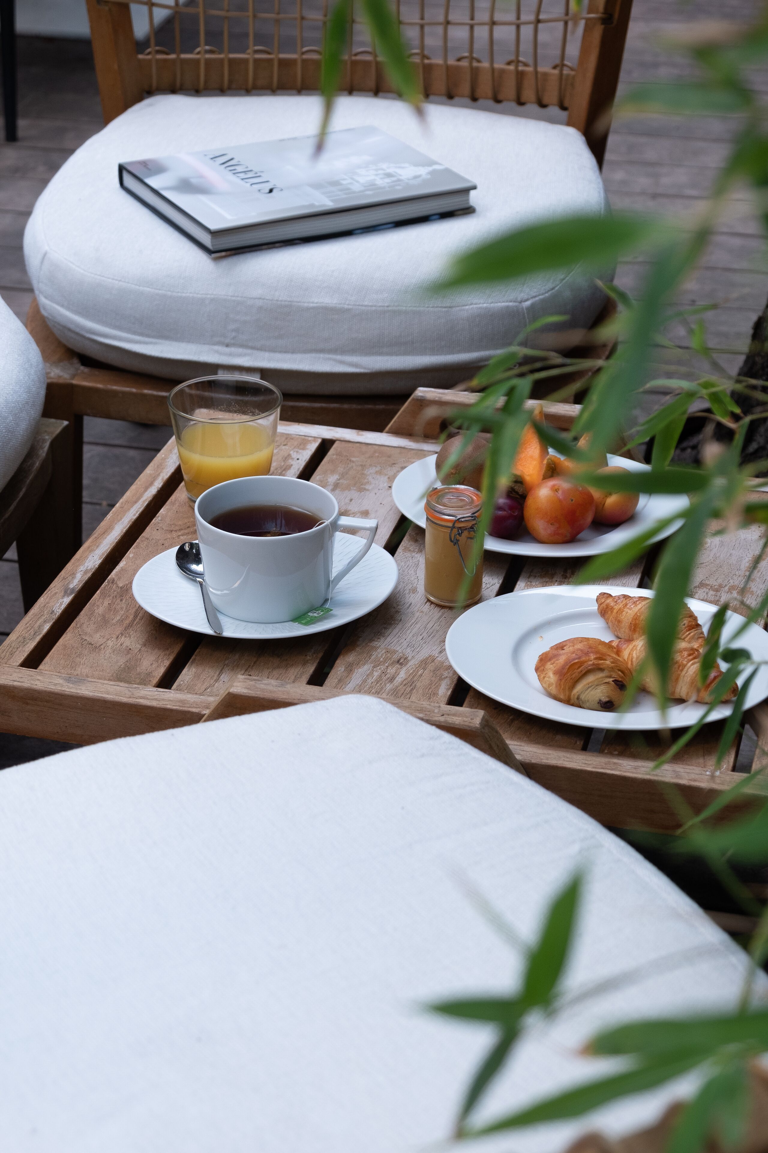 A wooden table with a cup of coffee, a glass of orange juice, a jar of jam, and a plate with croissants.