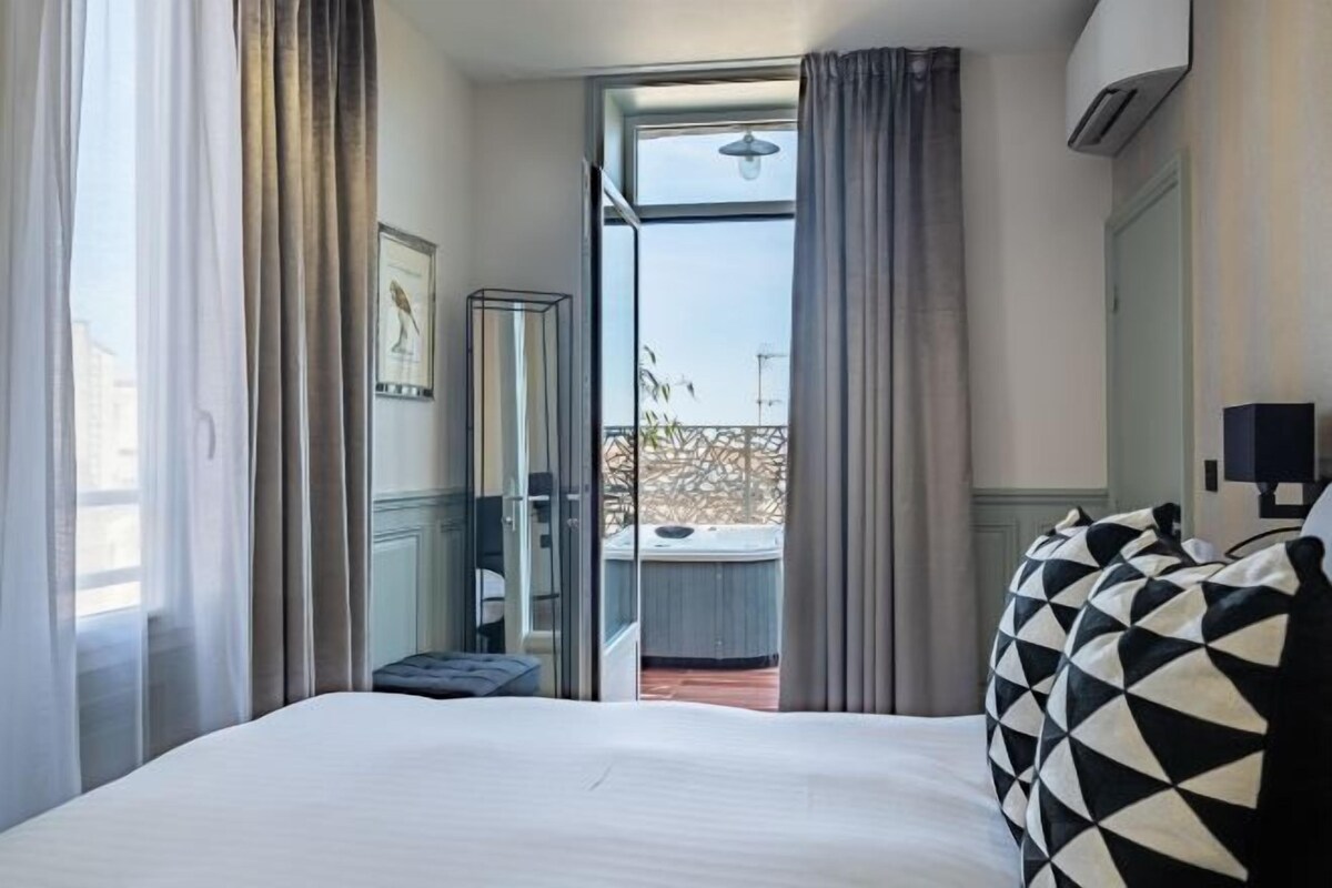 A hotel room with a bed, a large window, and a view of an outdoor area.