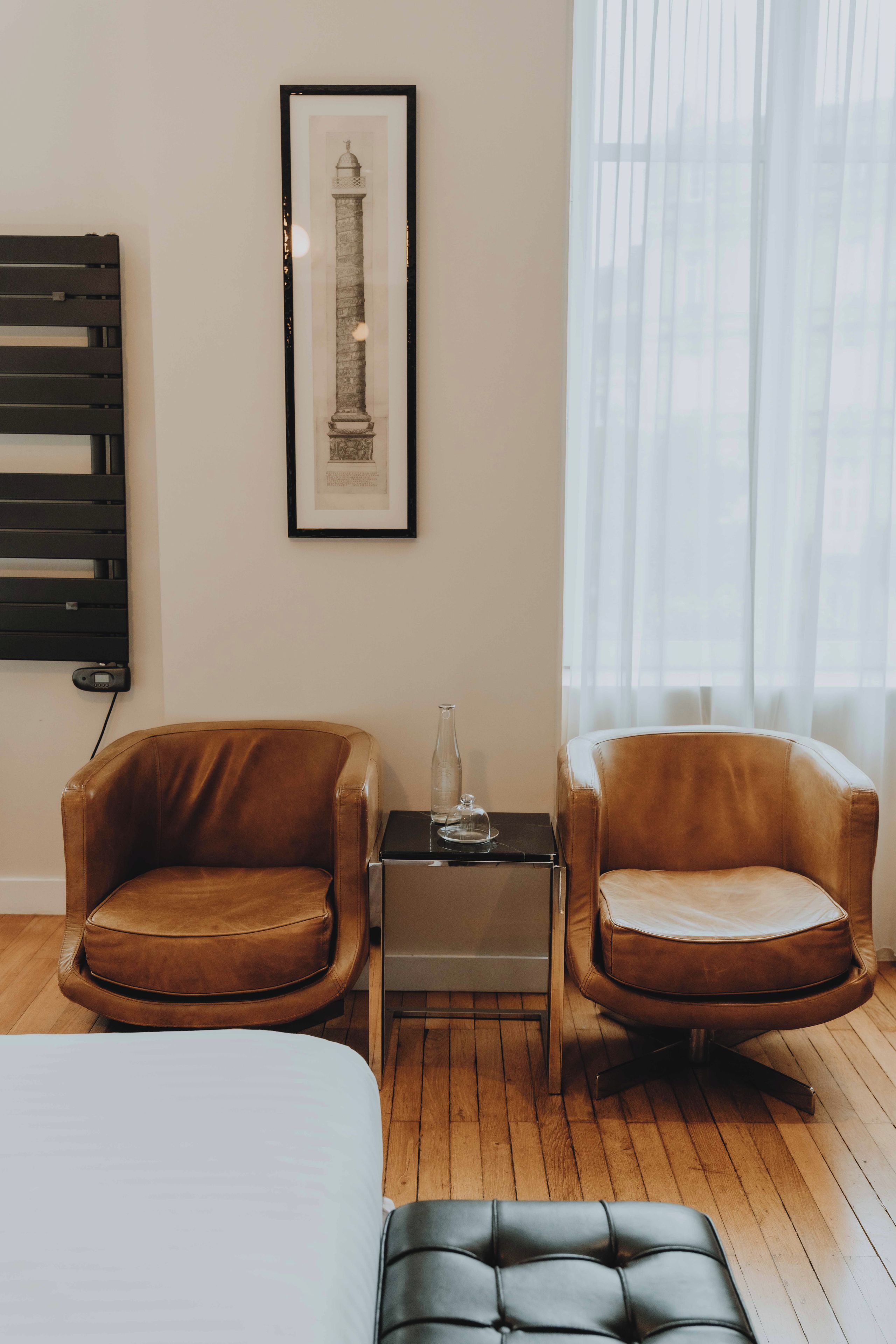 Una habitación con dos sillones de cuero, una mesita con un vaso y un cuadro enmarcado en la pared.