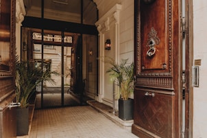 A grand entrance with a wooden door, a black metal gate, and two potted plants.
