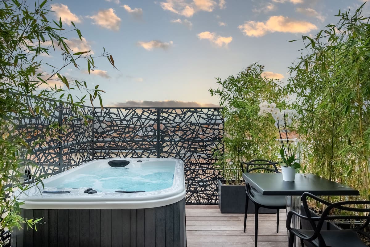 A hot tub on a wooden deck with a view of the sky and bamboo plants.