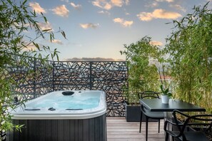 Un jacuzzi en una terraza de madera con vistas al cielo y plantas de bambú.