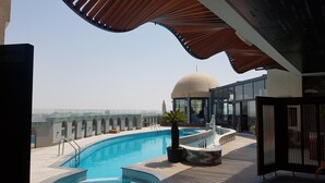Uma piscina no terraço com vista desobstruída para o horizonte urbano, um edifício moderno com cúpula e uma área de estar coberta.