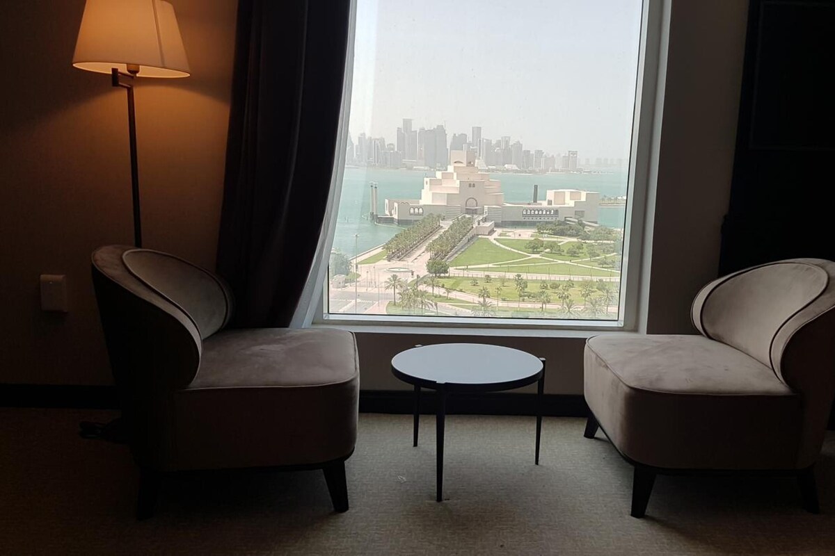 Une chambre d’hôtel avec deux fauteuils, une petite table et une vue sur le paysage urbain et l’eau.