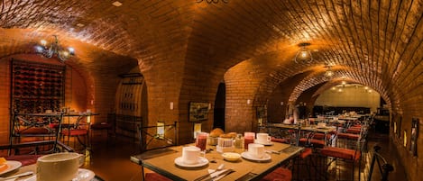 A restaurant with brick arches, tables set for dining, and a chandelier.