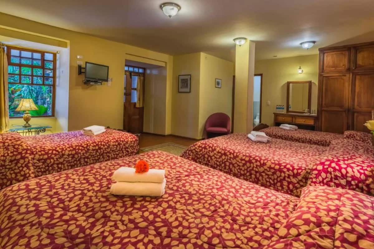 Une chambre d’hôtel avec quatre lits, une télévision, un miroir et une fenêtre avec des rideaux.