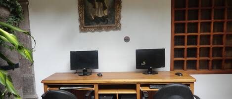 Un escritorio de madera con dos monitores, una computadora de escritorio, dos sillas y un cuadro en la pared.