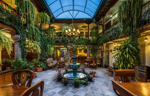A spacious atrium with a central fountain, surrounded by lush greenery and wooden furniture.