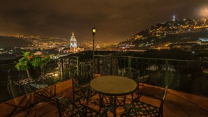 A rooftop terrace with a round table and chairs, overlooking a cityscape at night. - Hotel San Francisco de Quito (Quito)