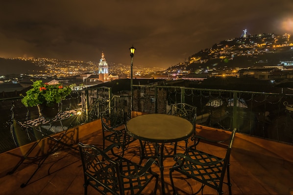A rooftop terrace with a round table and chairs, overlooking a cityscape at night. - Hotel San Francisco de Quito (Quito)